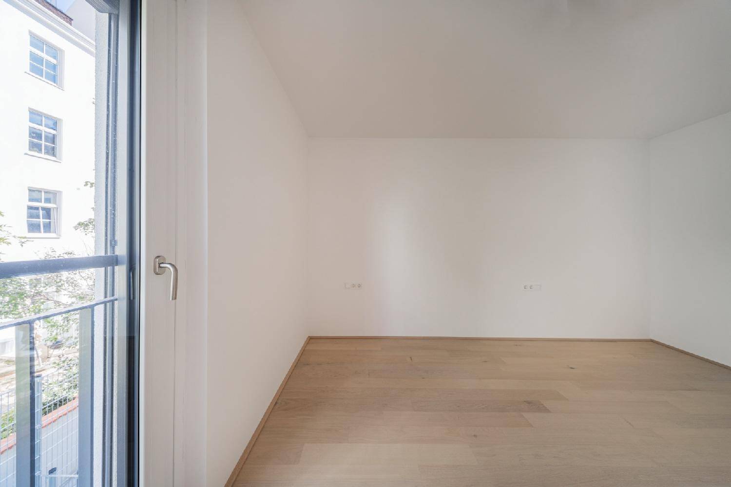 Helles Zimmer mit Holzboden und einem französischen Balkon, der einen Blick nach draußen bietet.
