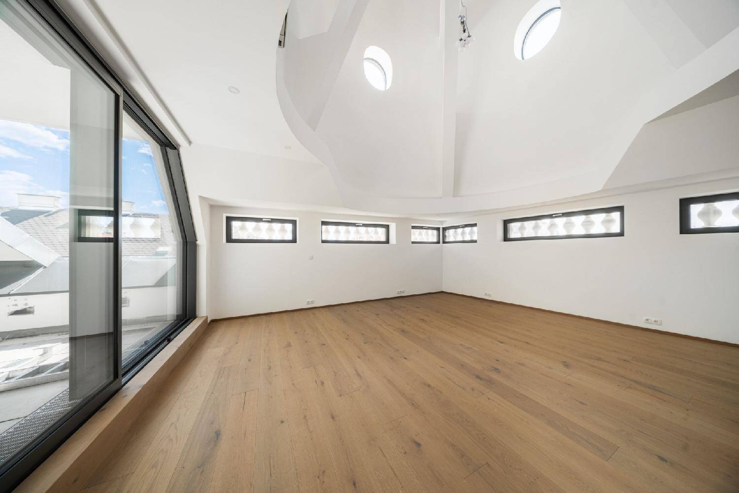 Heller Wohnraum mit Holzboden, gewölbter Decke, Oberlichtern und großen Fenstern für viel Tageslicht.