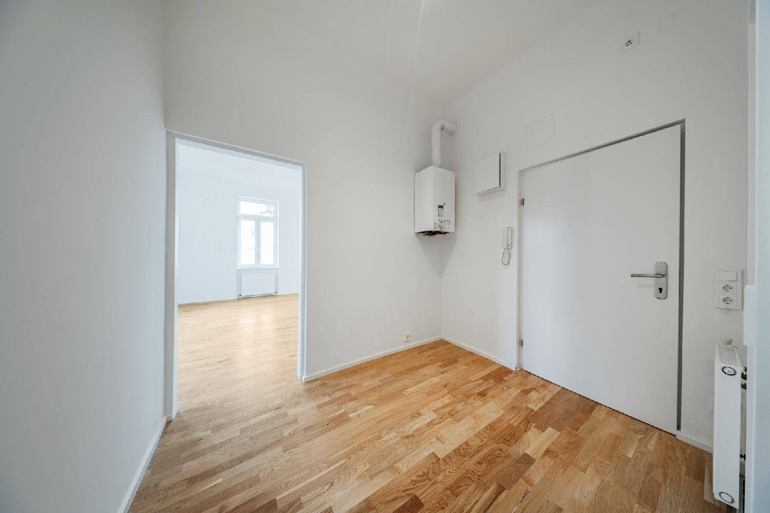 Heller Flur mit Holzboden und Heizungsanlage, der zu den verschiedenen Zimmern der Wohnung führt.