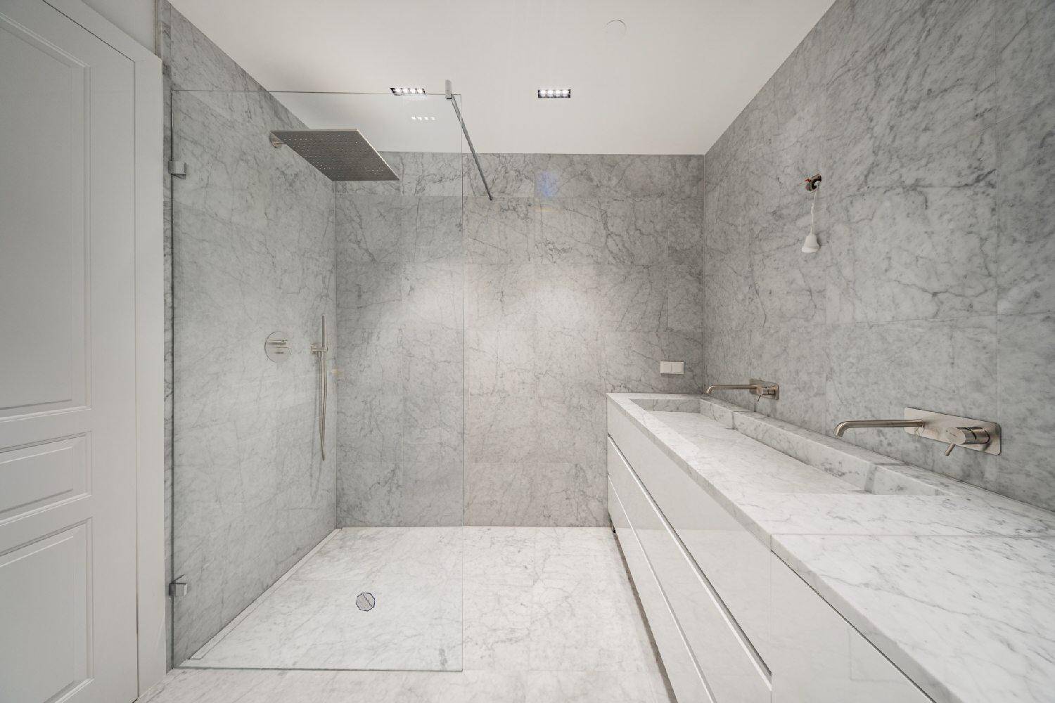 Luxuriöses Badezimmer mit Marmorfliesen, begehbarer Dusche und Doppelwaschbecken.