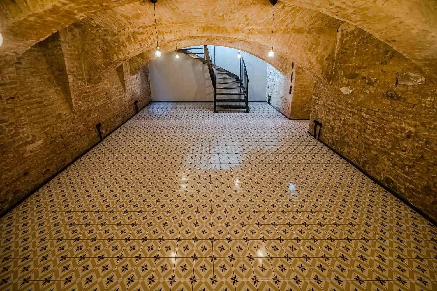 Historischer Gewölbekeller mit freigelegten Ziegelwänden, gemusterten Fliesen und einer Wendeltreppe.
