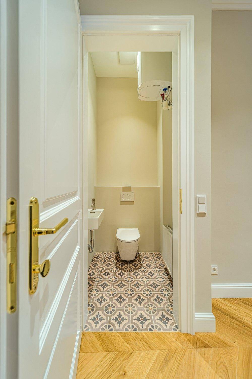 Modernes Gäste-WC mit Wand-WC, kleinem Waschbecken und gemusterten Fliesenboden, durch eine Tür sichtbar.