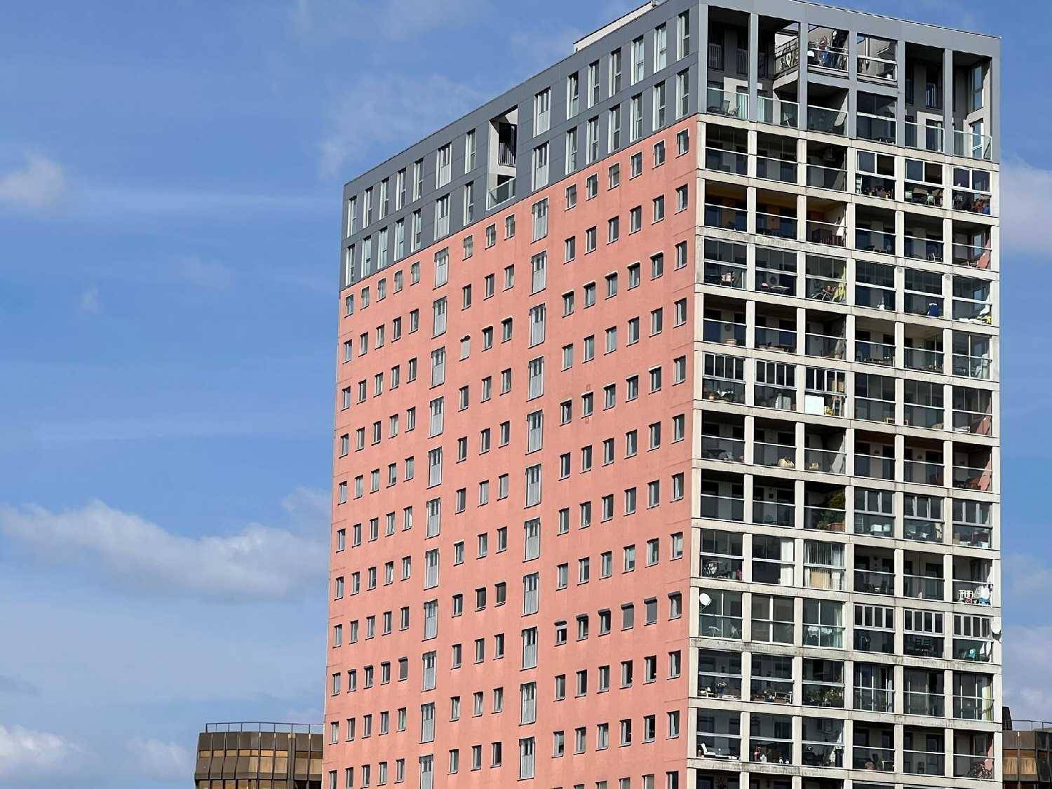 Modernes Hochhaus mit markanter rosa Fassade und zahlreichen Balkonen, die einen urbanen Lebensstil versprechen.