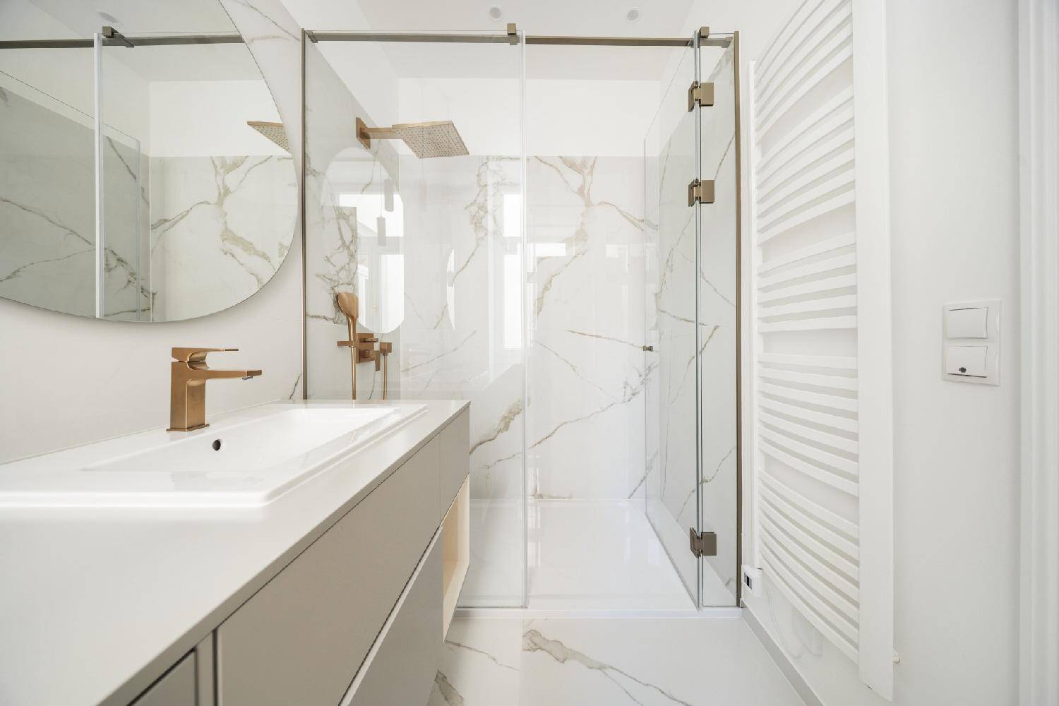 Elegantes Badezimmer mit Marmoroptik, Glasdusche und modernem Heizkörper.