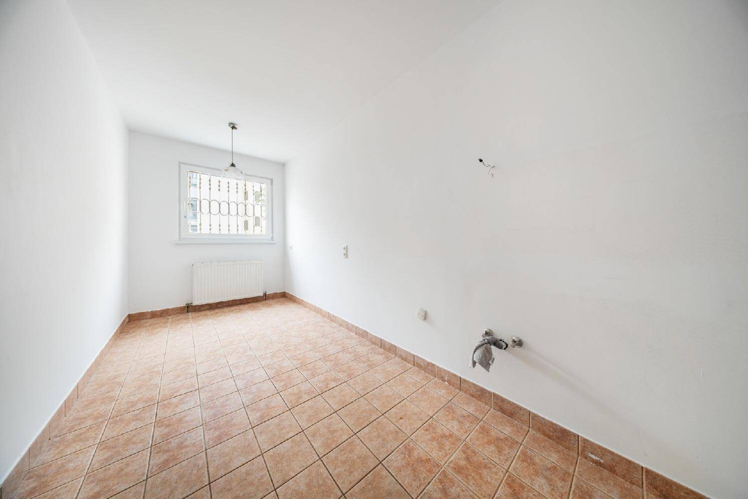Leere Küche mit Terrakotta-Fliesenboden und Fenster, bereit für die Installation einer Einbauküche.