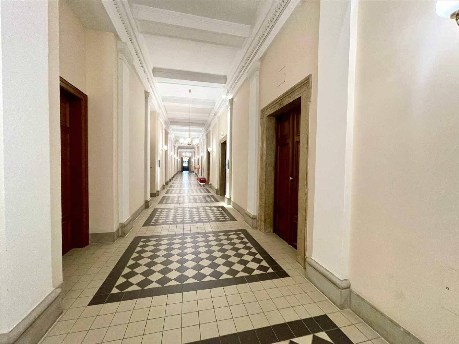 Langer Flur mit Schachbrettmuster-Fliesenboden und hohen Decken in einem historischen Gebäude.
