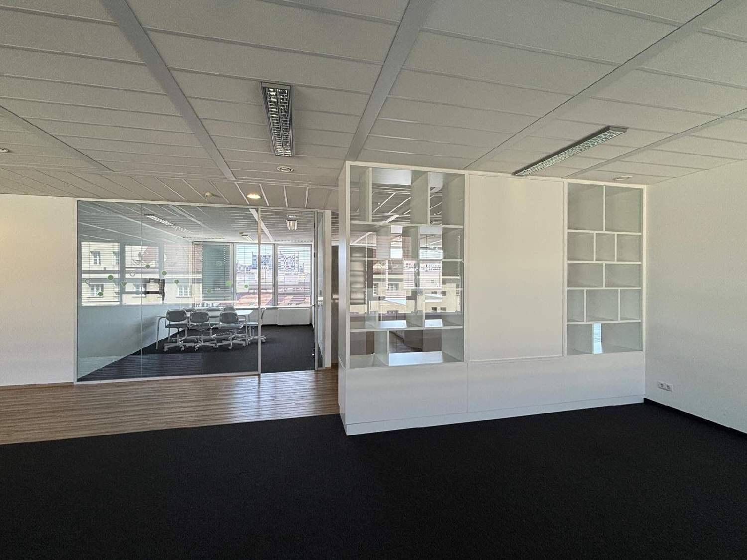 Helles Büro mit Teppichboden, Glaswänden und Blick auf einen Konferenzraum, ideal für moderne Arbeitsumgebungen.