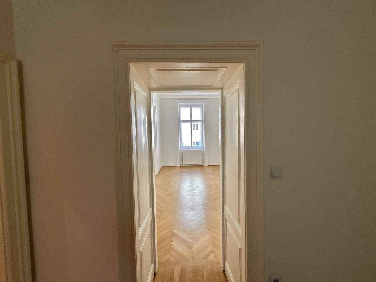 Durchgang zu einem weiteren hellen Zimmer mit Fischgrätparkett und einem großen Fenster, typisch für Altbauwohnungen.