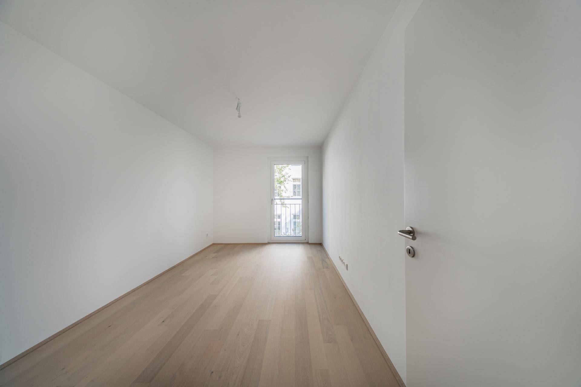 Unmöbliertes Zimmer mit hellem Holzboden und französischem Balkon.