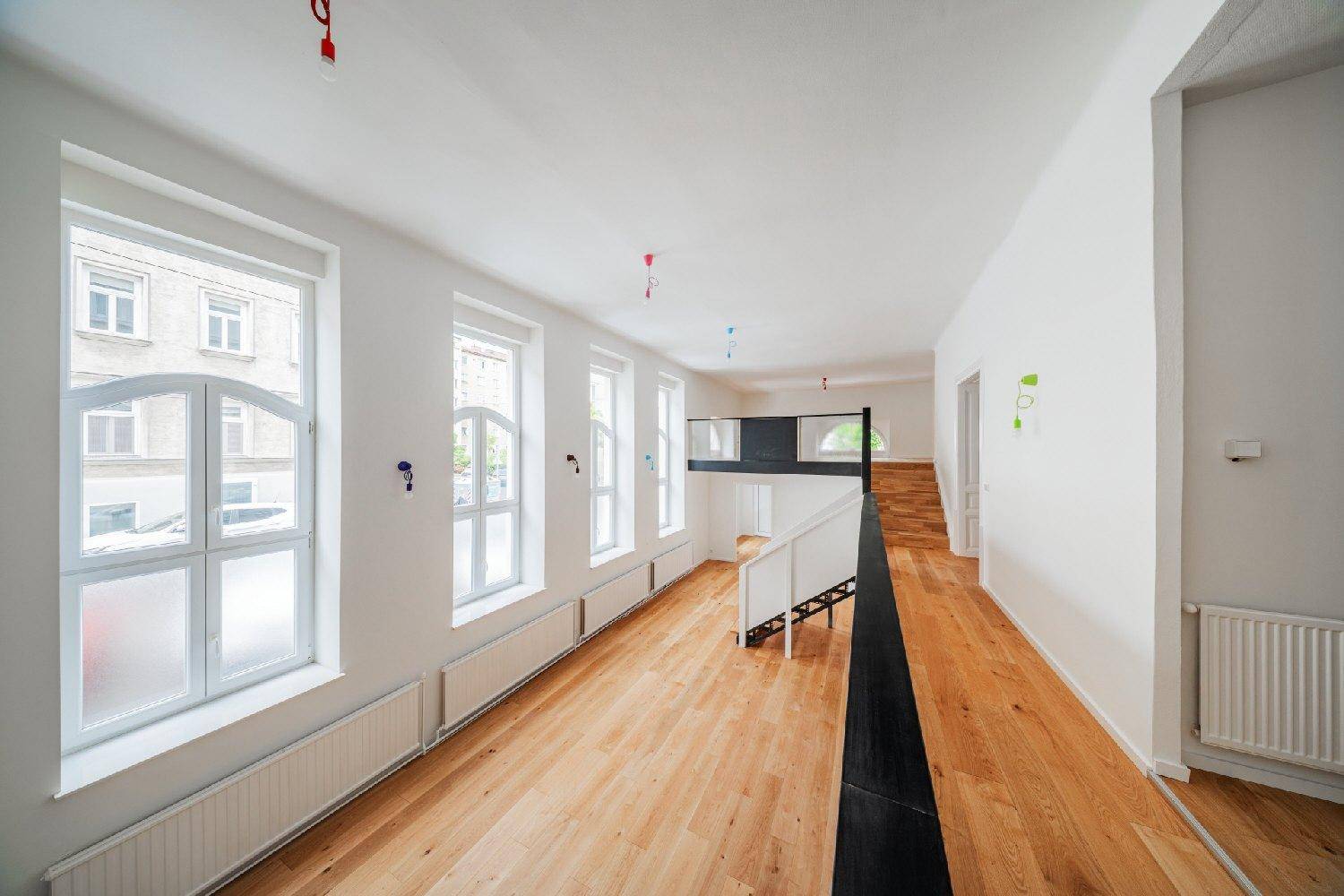 Offener Wohnbereich mit Holzboden, hohen Fenstern und einer Galerie, die den Raum strukturiert.