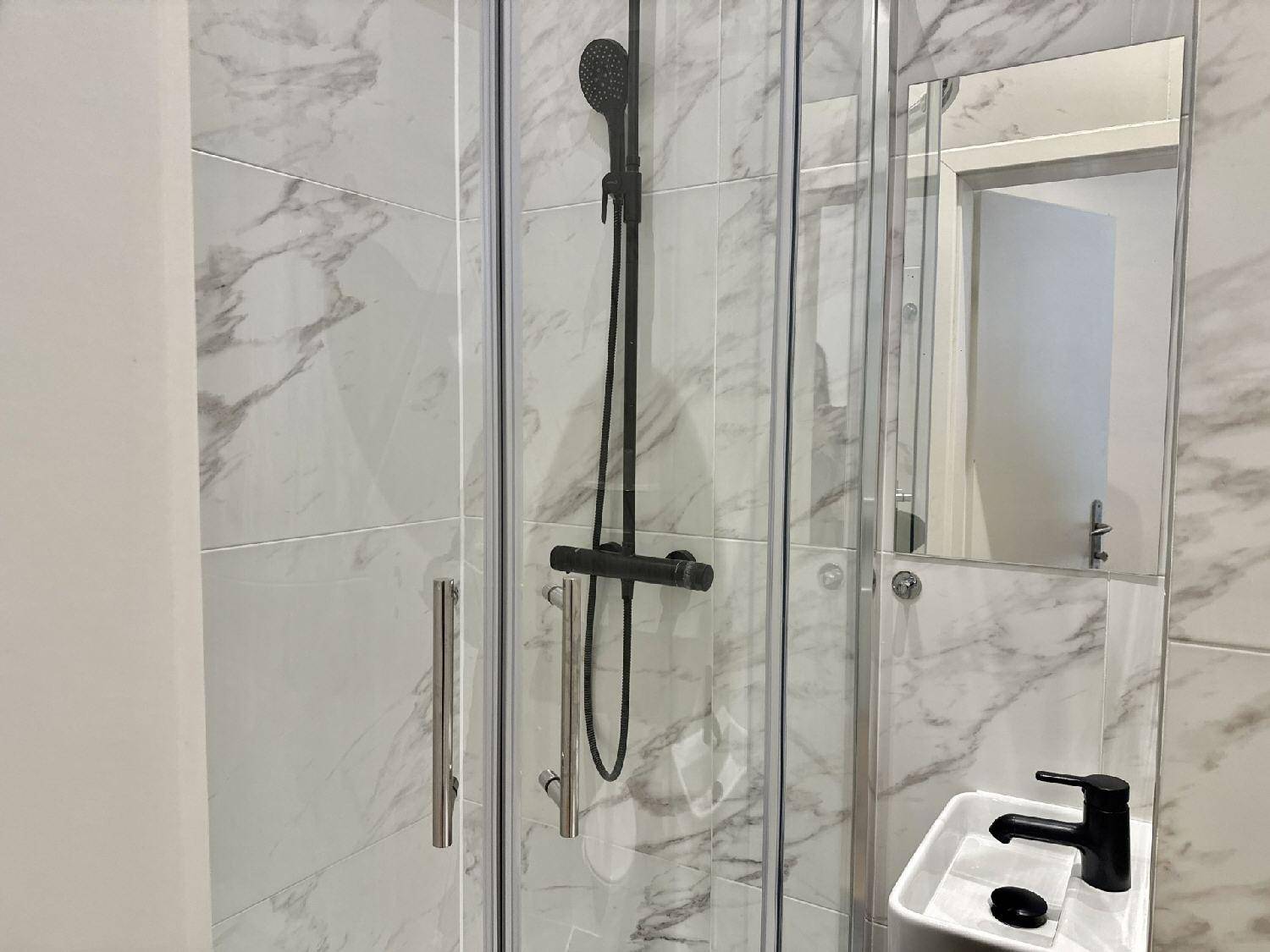 Detailansicht der modernen Duschkabine und des Einzelwaschbeckens mit schwarzer Armatur im Badezimmer.
