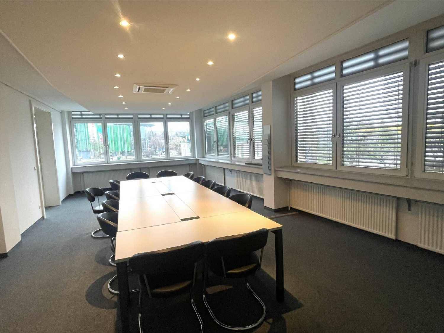 Geräumiger Konferenzraum mit großem Tisch, vielen Stühlen und hellen Fenstern mit Jalousien.