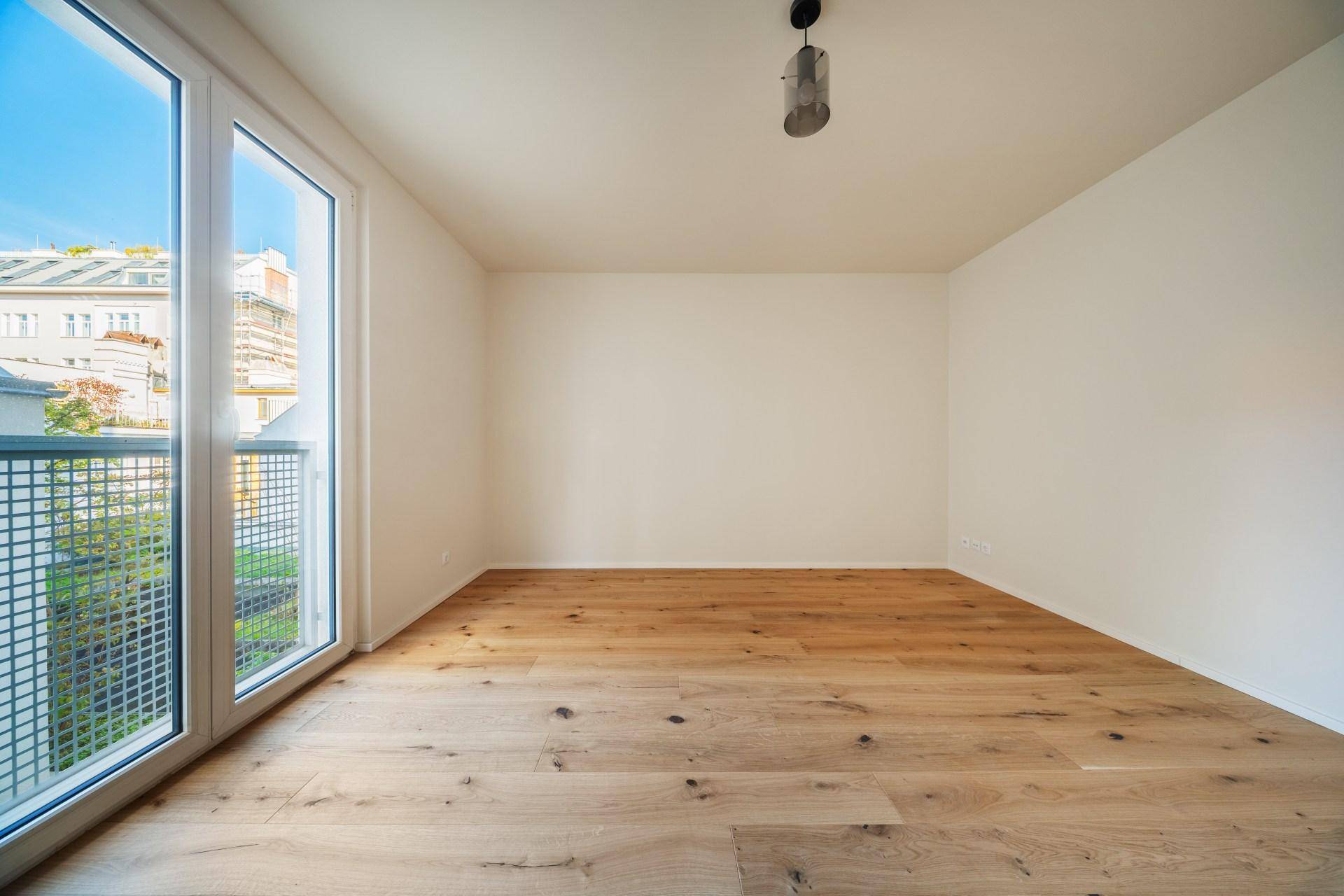 Lichtdurchflutetes Zimmer mit Holzboden und bodentiefen Fenstern, die einen Blick nach draußen bieten.