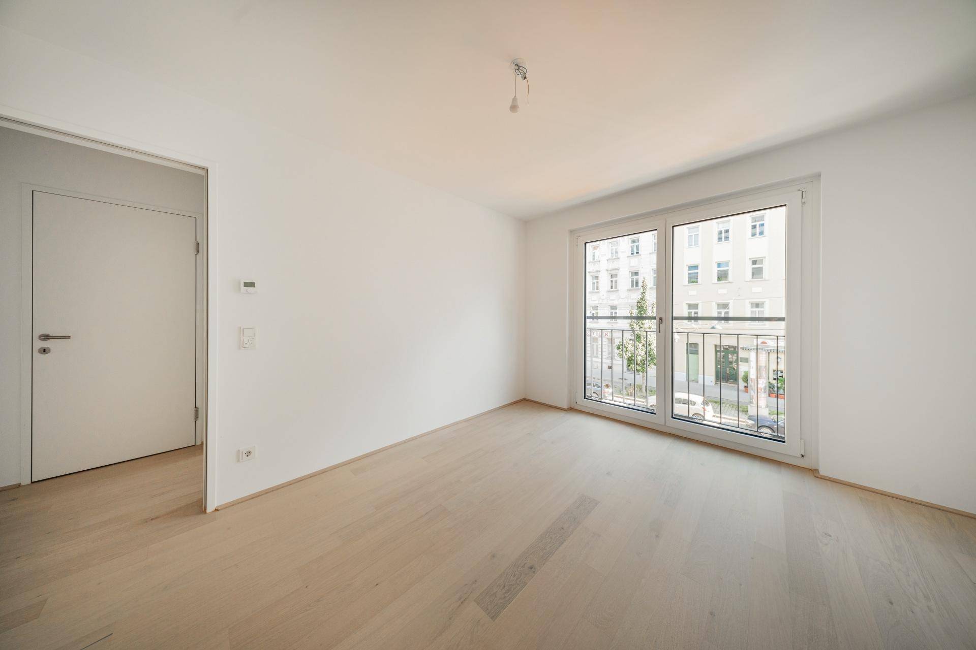 Helles Zimmer mit Parkettboden und Blick auf die Straße, ideal als Schlaf- oder Arbeitszimmer.