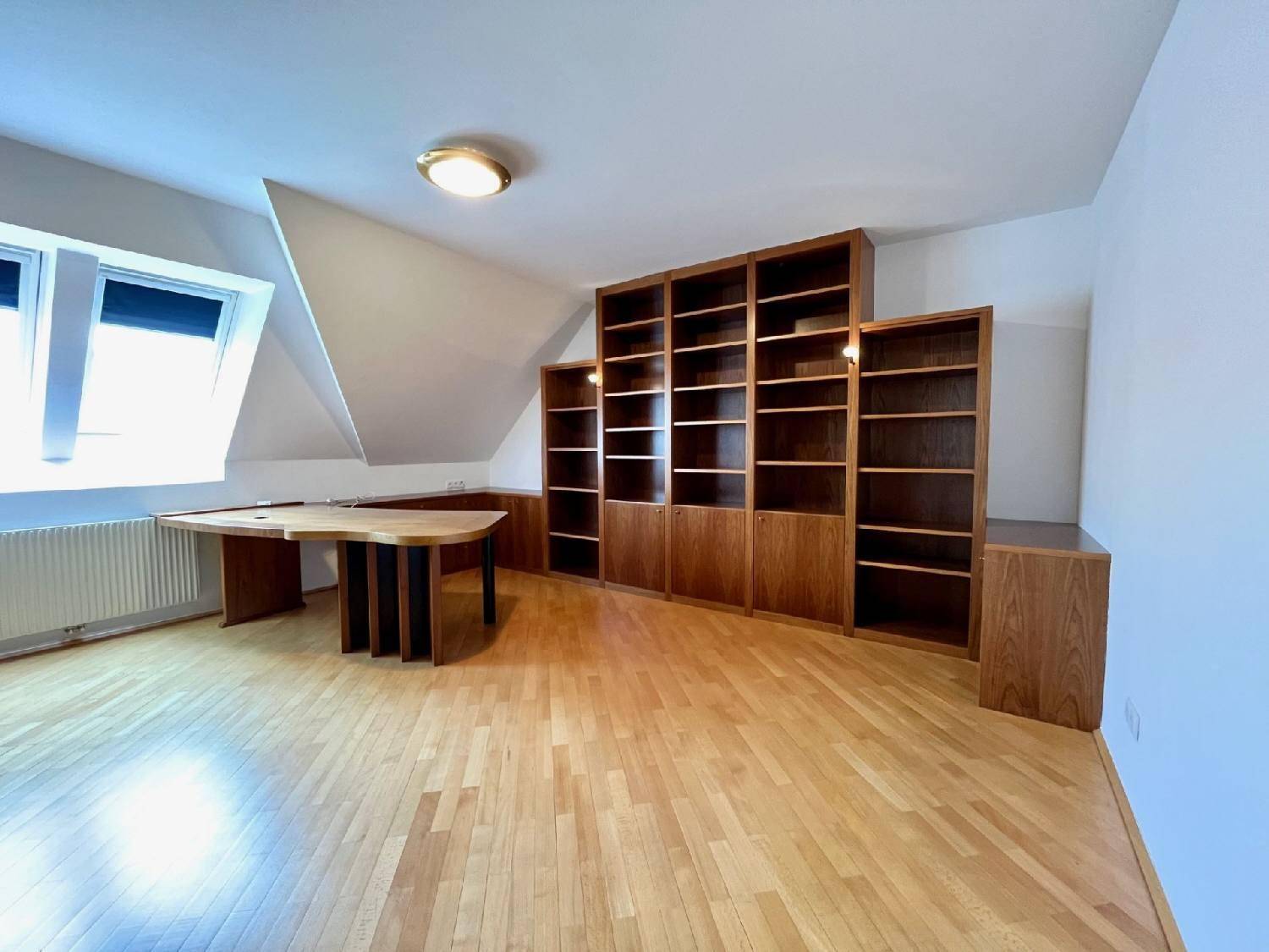 Ruhiges Arbeitszimmer mit Holzboden, Einbauregalen und einem großen Schreibtisch unter dem Fenster.