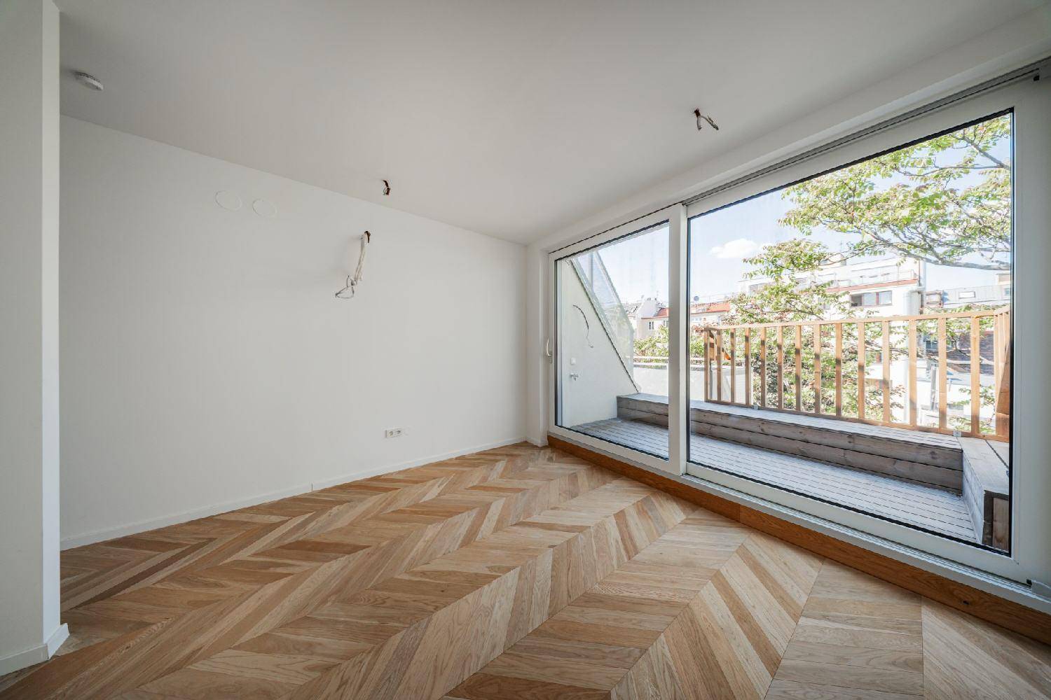 Geräumiges Zimmer mit hellem Fischgrätparkett und großen Schiebetüren zur sonnigen Terrasse.