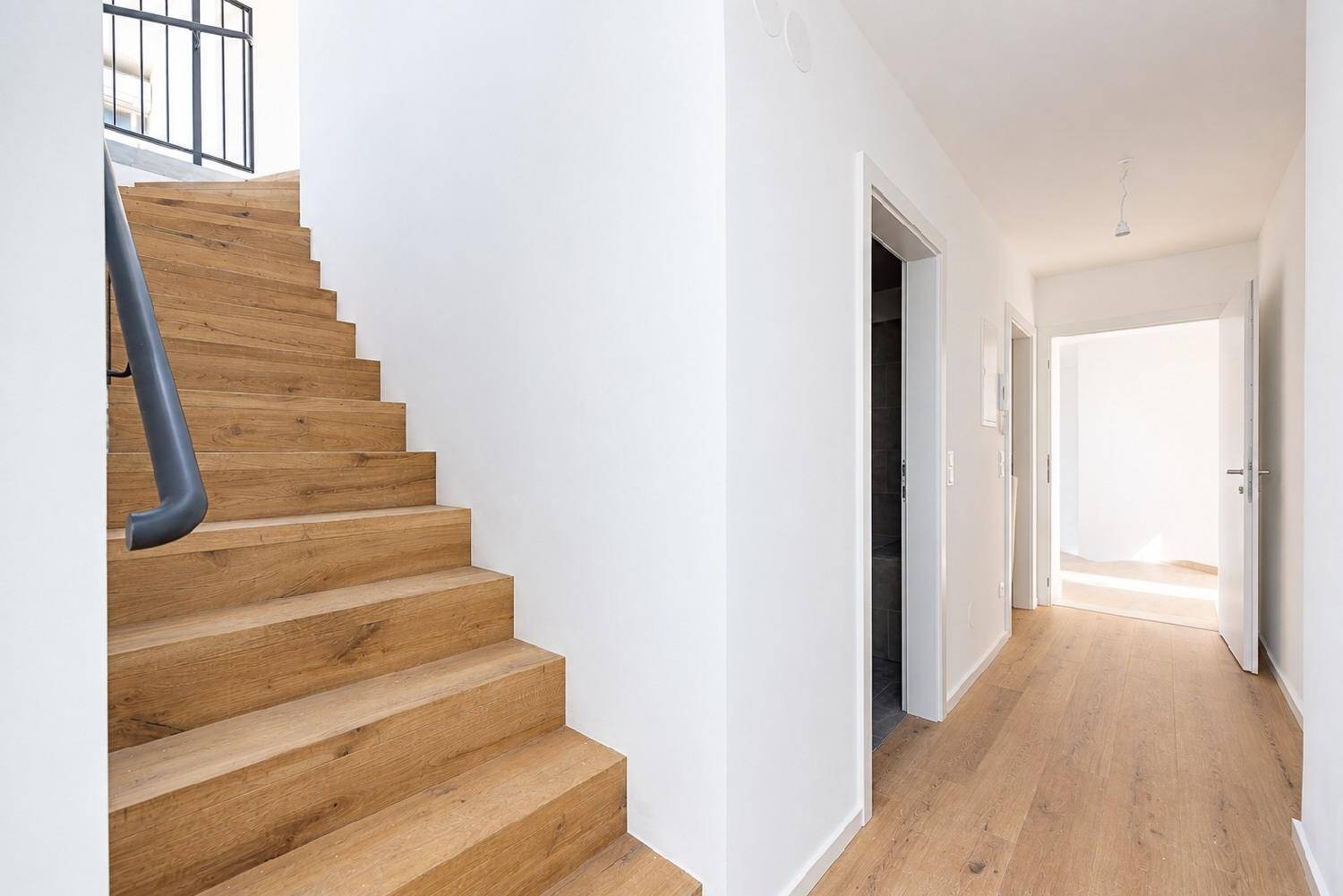Moderner Flur mit Holztreppe und hellem Holzboden, führt zu weiteren Räumen im Obergeschoss.