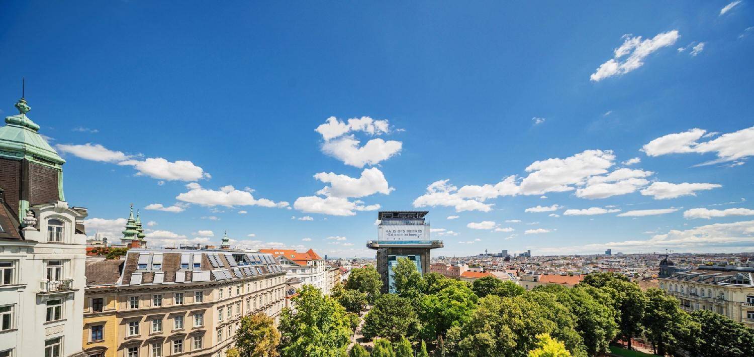 Panoramablick über die Stadt mit historischer Architektur, grünen Bäumen und blauem Himmel an einem sonnigen Tag.