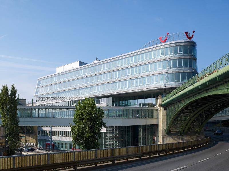Modernes Bürogebäude mit geschwungener Glasfassade und angrenzender Brückenkonstruktion unter blauem Himmel.