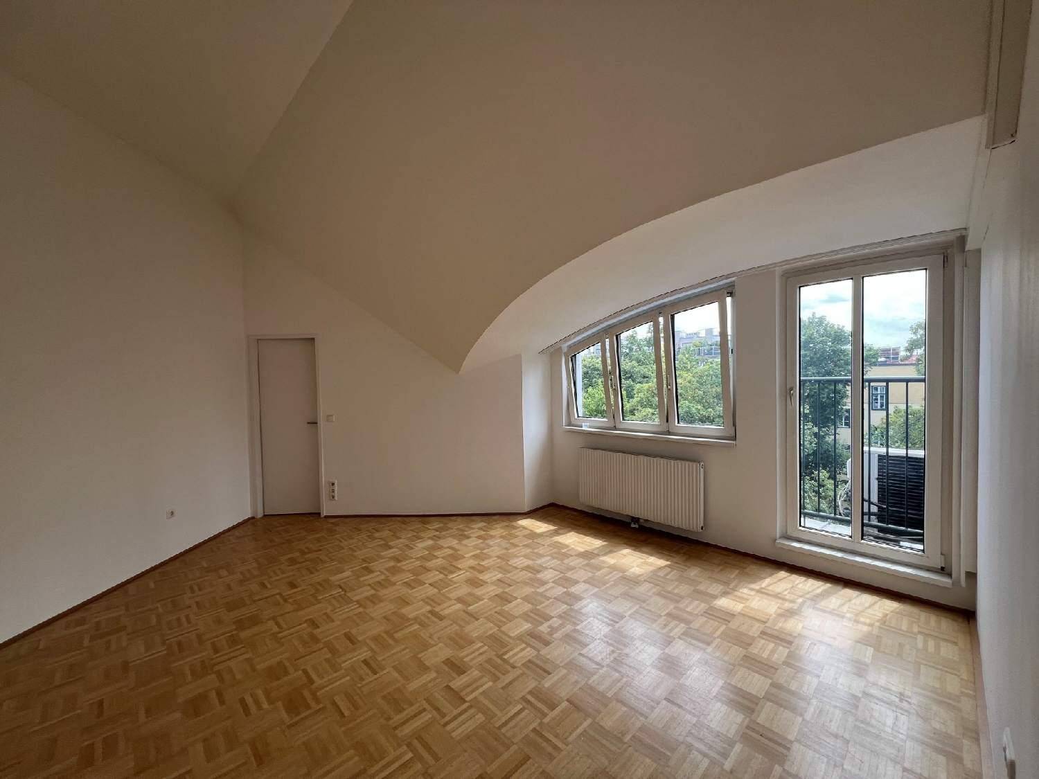 Heller Wohnraum mit Parkettboden, Dachschrägen und Fensterfront zum Außenbereich.