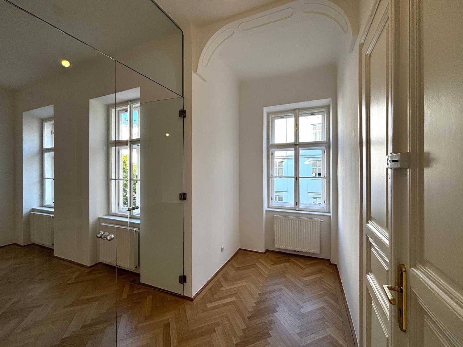 Heller Raum mit Fischgrätparkett, einem Fenster und einer modernen Glasabtrennung.