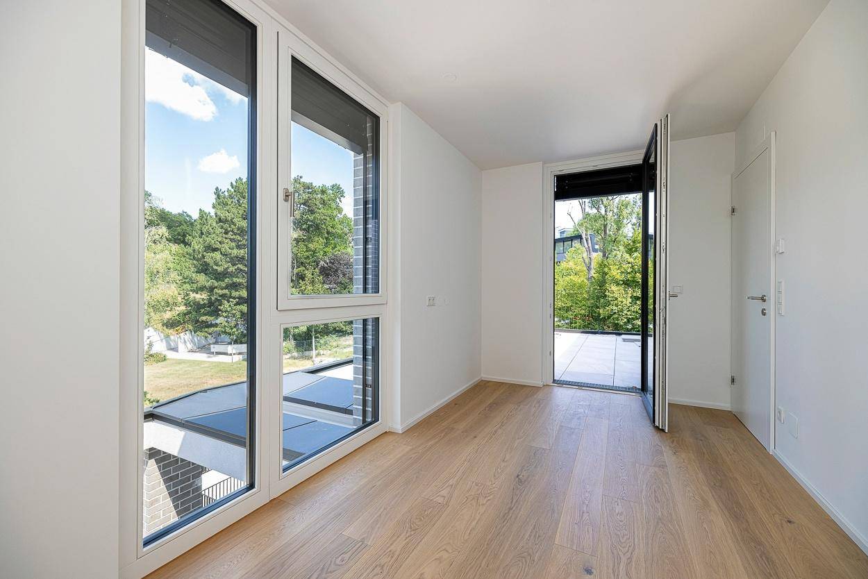 Helles Schlafzimmer mit Holzboden und Zugang zu einem Außenbereich mit Grünblick.