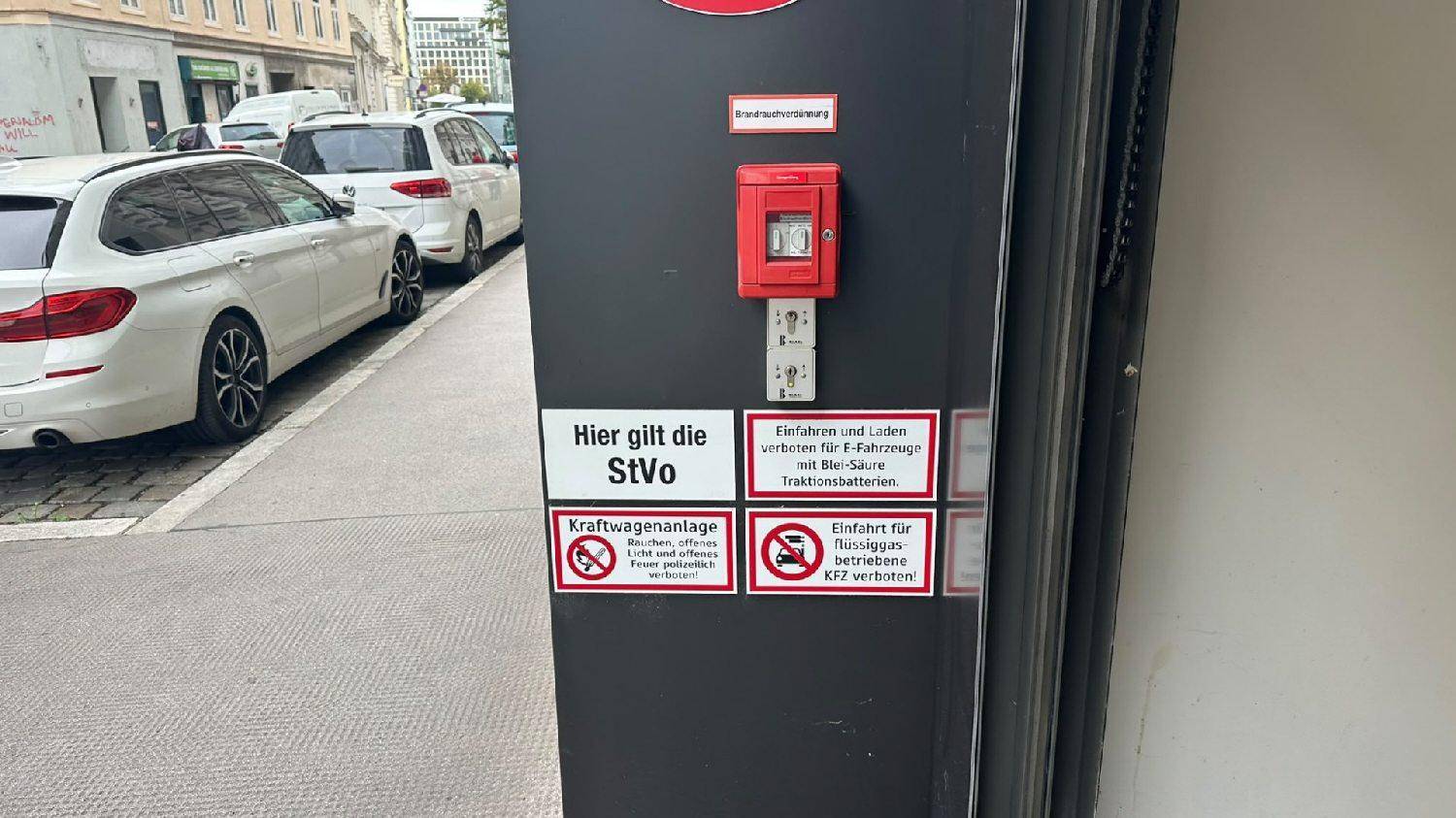 Hinweisschilder an einem Garageneingang mit geparkten Autos auf der Straße im Hintergrund.