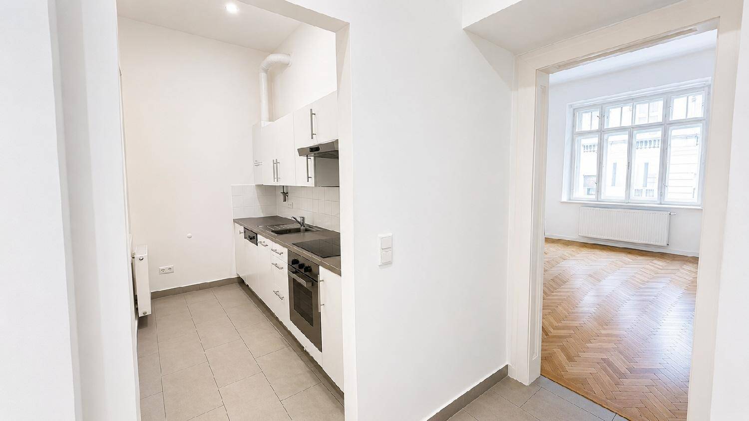 Kleine, funktionale Küche mit weißen Schränken und Blick in ein weiteres Zimmer.