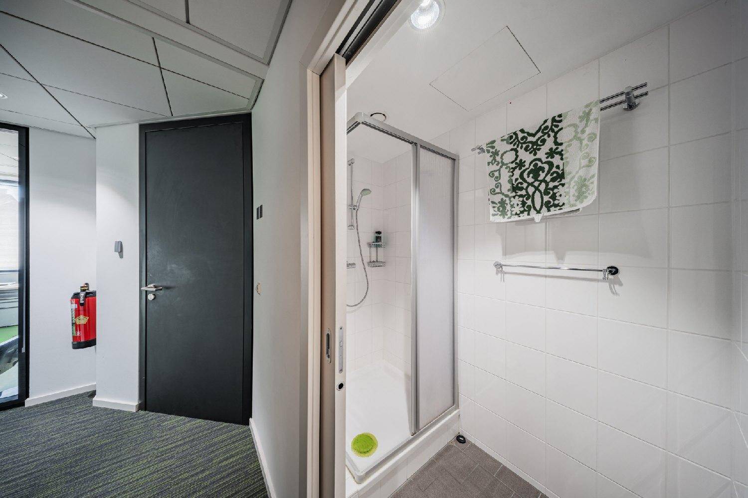 Kleines Badezimmer mit Duschkabine, weißen Fliesen und grauen Bodenfliesen.