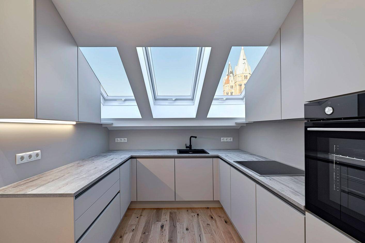 Moderne Küche mit Dachfenstern, Holzarbeitsplatte und Blick auf den Kirchturm.