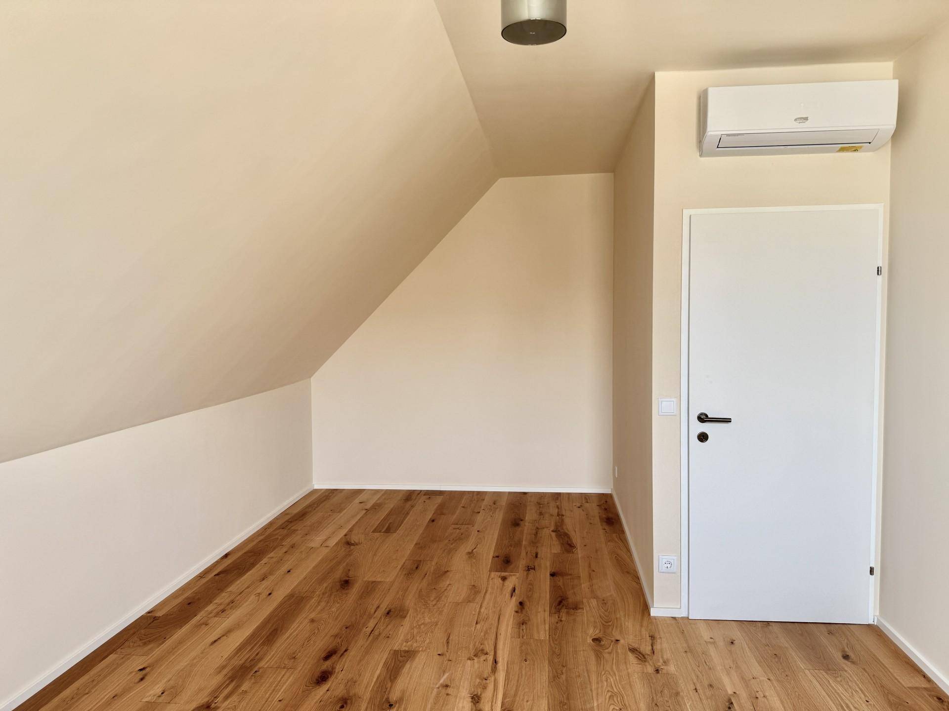 Zimmer mit Holzboden, Dachschräge, weißer Tür und installierter Klimaanlage.