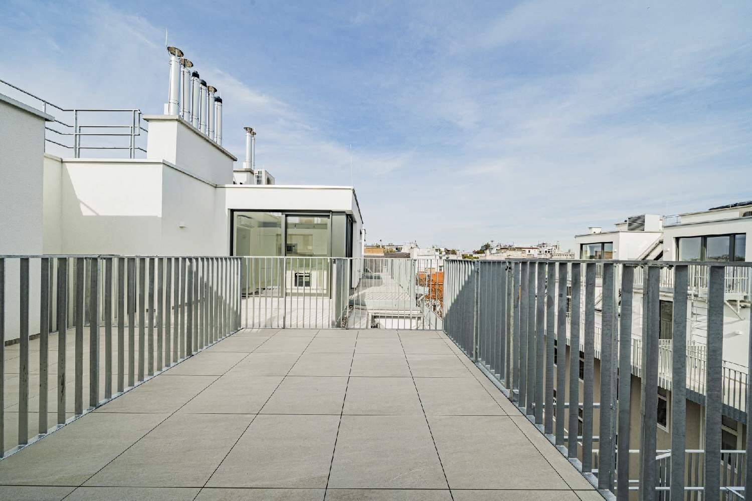 Geräumige Dachterrasse mit Fliesenboden und modernem Geländer, umgeben von urbaner Architektur.