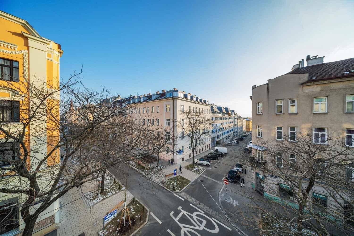 Weitläufiger Blick über eine städtische Kreuzung mit Gebäuden und Bäumen unter blauem Himmel.