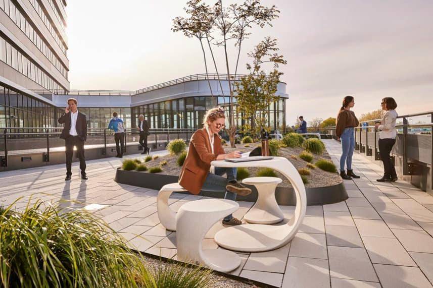 Sonniger Außenbereich auf einer Terrasse mit modernen Sitzgelegenheiten und Menschen, die arbeiten oder sich unterhalten.