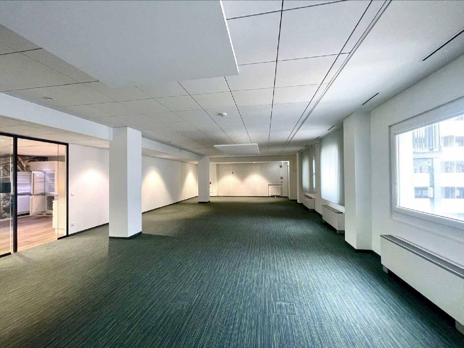 Großes, leeres Büro mit Teppichboden, Säulen und Fenstern mit Jalousien.