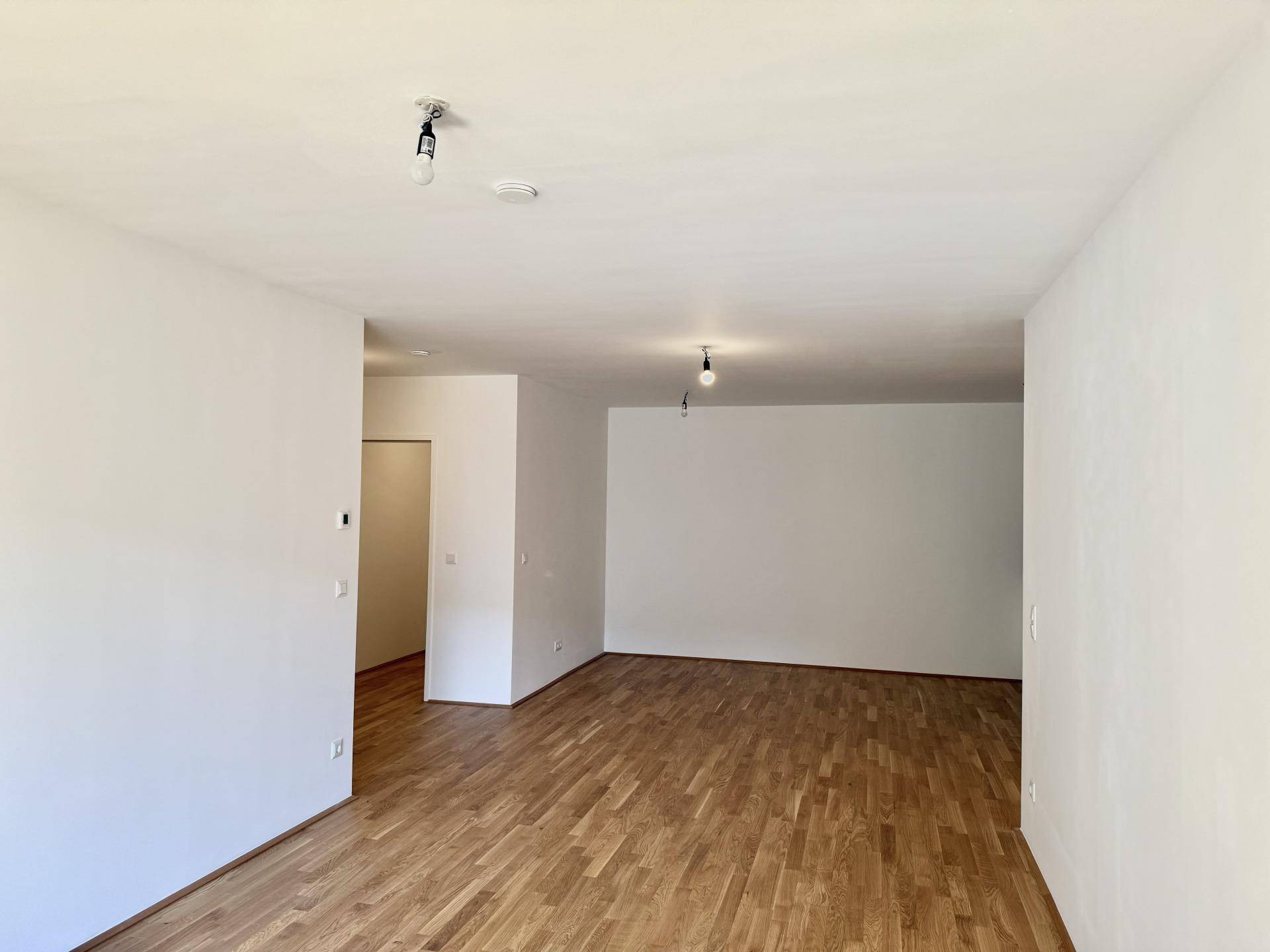 Geräumiger, leerer Raum mit hellem Parkettboden und weiß gestrichenen Wänden, vielseitig nutzbar.