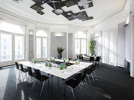 Großer, heller Konferenzraum mit mehreren Tischen, Stühlen und dekorativer Decke.