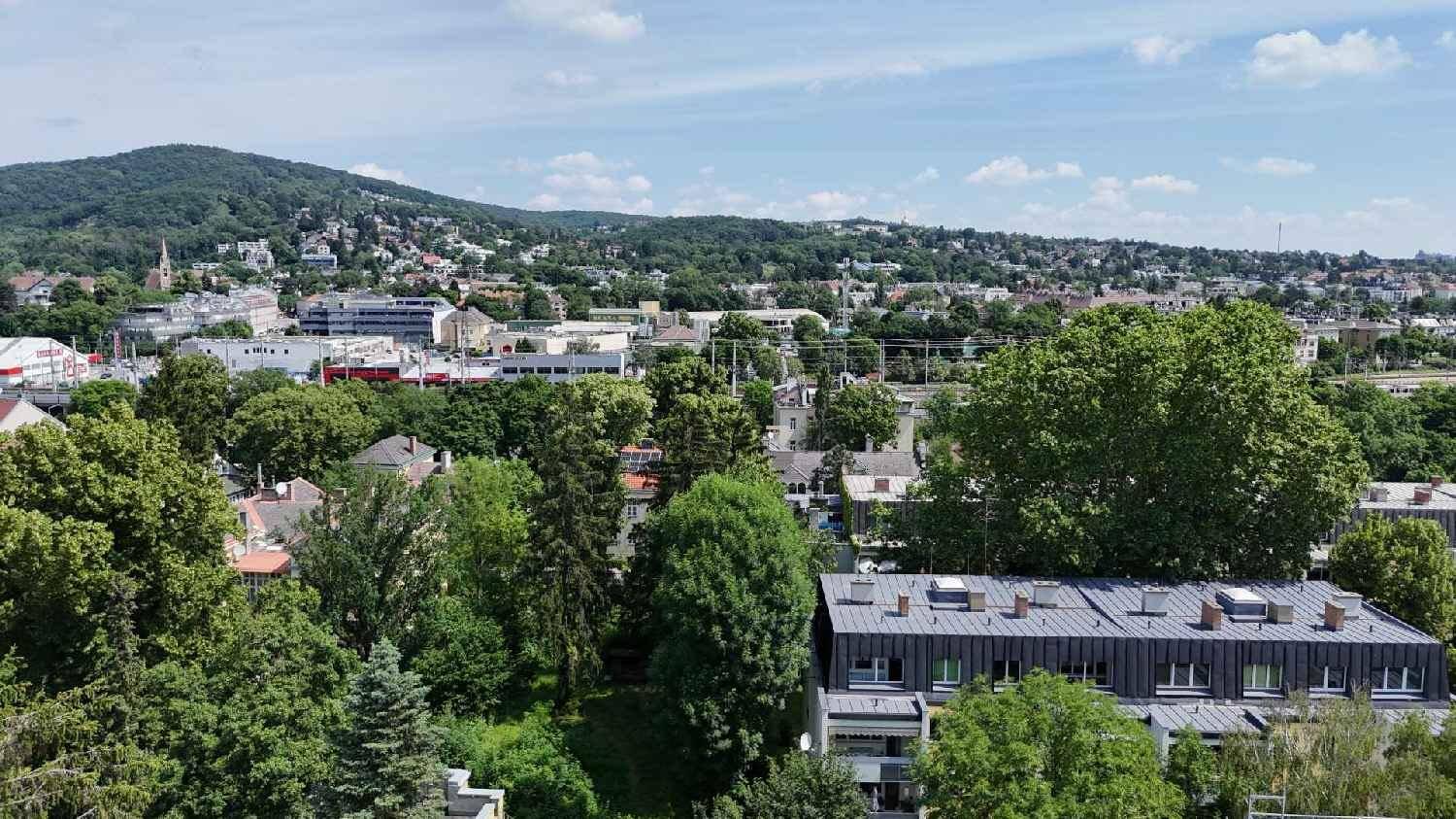 Panoramablick über eine grüne Stadtlandschaft mit bewaldeten Hügeln im Hintergrund.