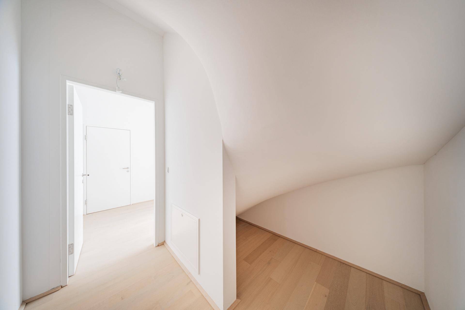 Heller Flur mit geschwungener Decke und hellem Holzfußboden in einem modernen Gebäude.