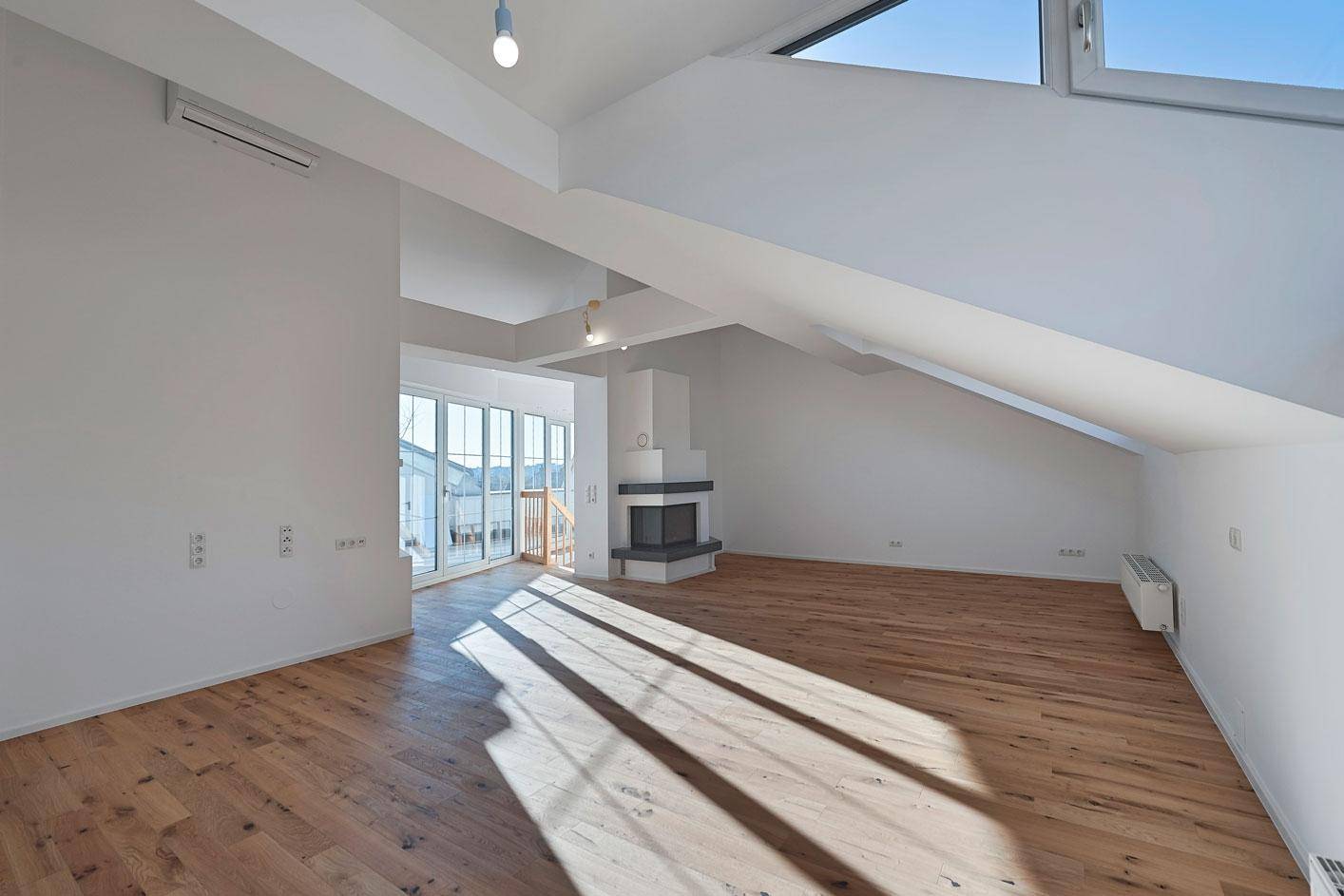 Geräumiges Dachgeschosszimmer mit Holzboden, Kamin und Zugang zur Terrasse.