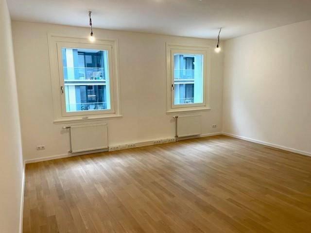 Helles Zimmer mit zwei großen Fenstern, Holzfußboden und weißen Wänden, bereit zur Einrichtung.