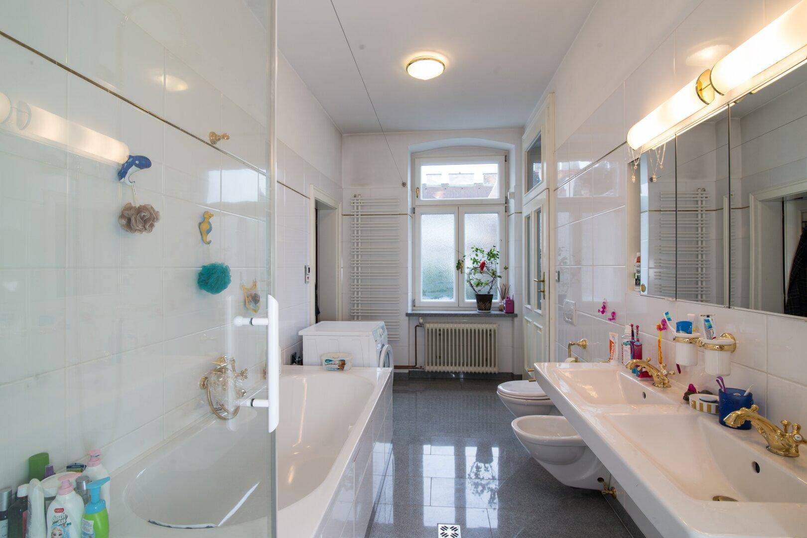 Helles Badezimmer mit Badewanne, Doppelwaschbecken und Fenster für natürliche Belüftung.