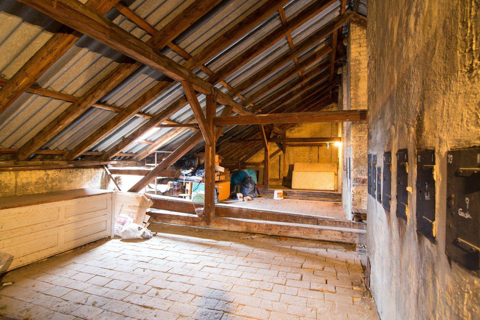 Unausgebauter Dachboden mit sichtbaren Holzbalken und Ziegelboden, ideal für zukünftigen Ausbau.