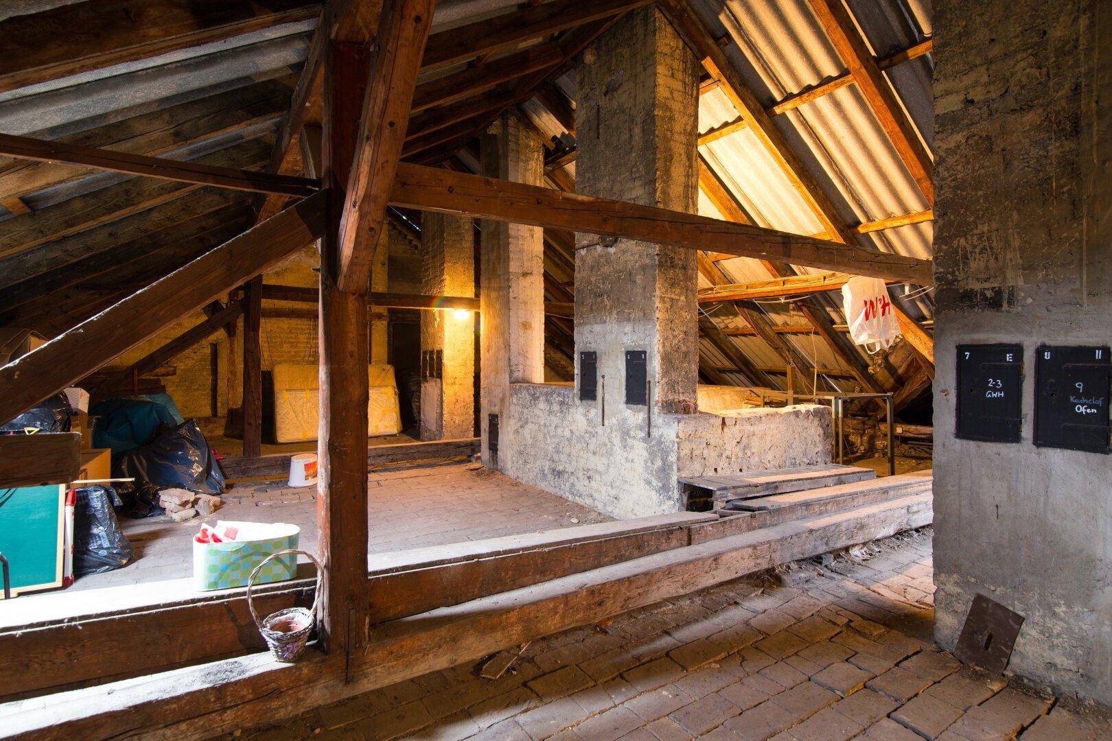 Unausgebauter Dachboden mit sichtbaren Holzbalken und Ziegelwänden, bereit für den Ausbau.