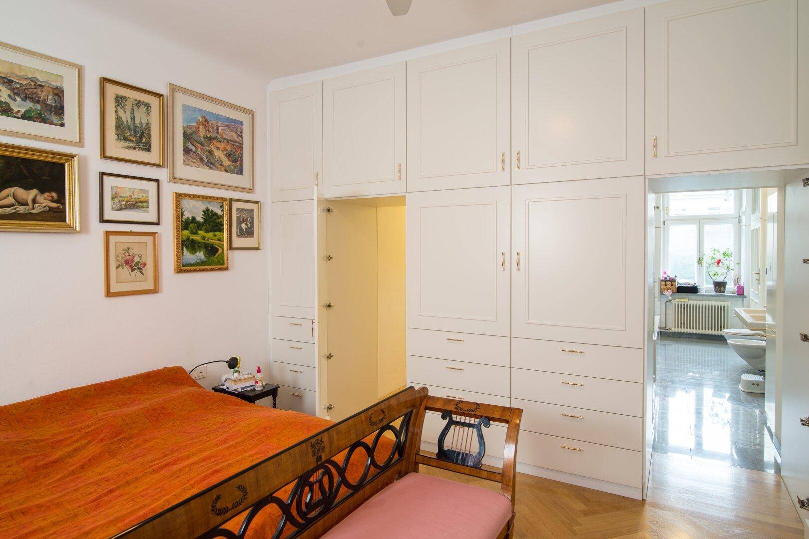Helles Schlafzimmer mit maßgefertigten Einbauschränken, Parkettboden und direktem Zugang zum Badezimmer.