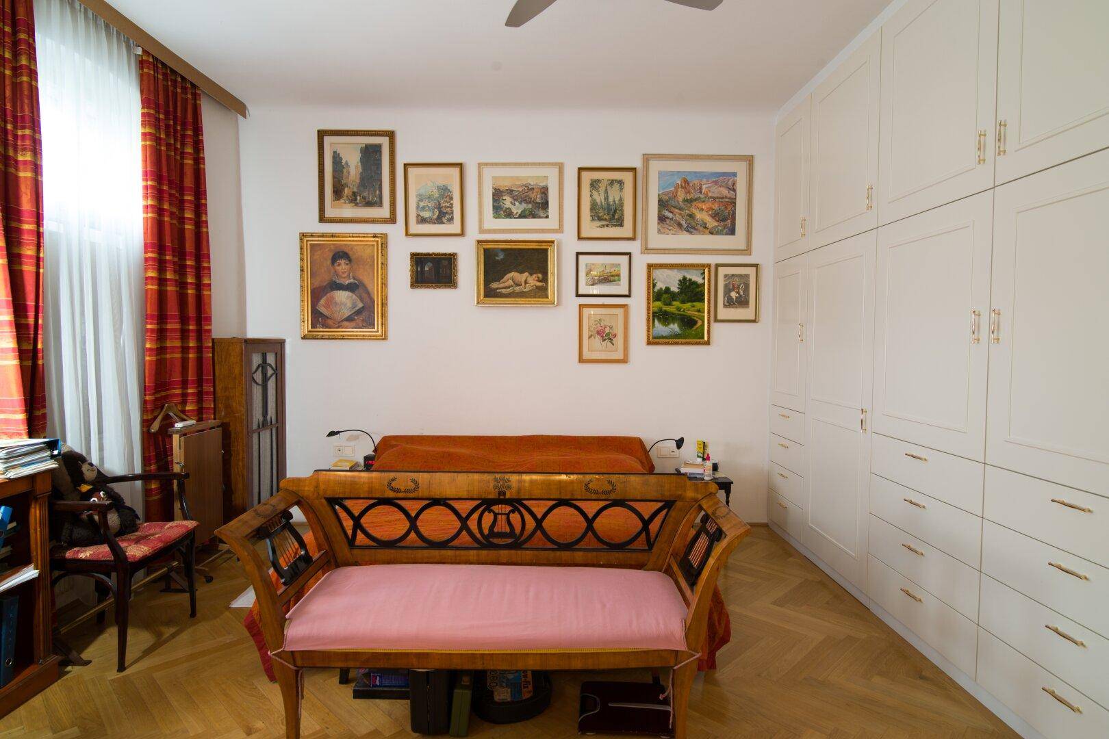 Schlafzimmer mit Einbauschränken, Parkettboden und einer Sammlung von Kunstwerken an der Wand.