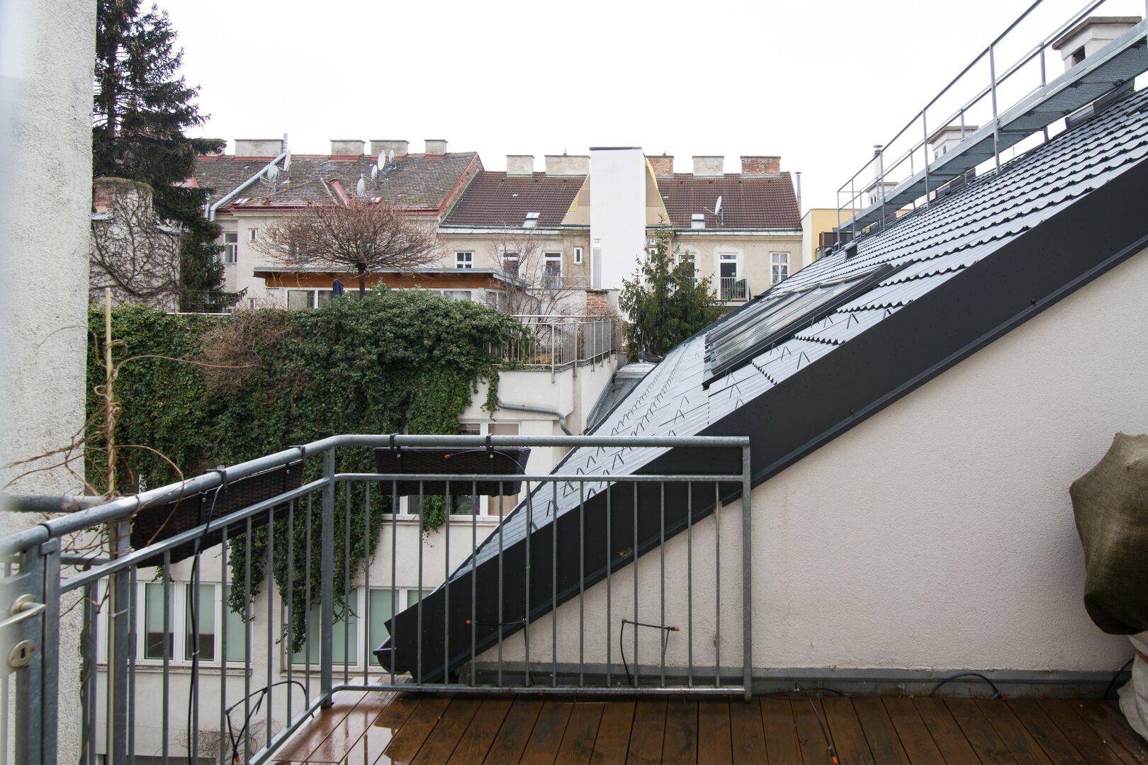 Balkon mit Holzboden und Blick auf die umliegenden Dächer und Gebäude unter bewölktem Himmel.