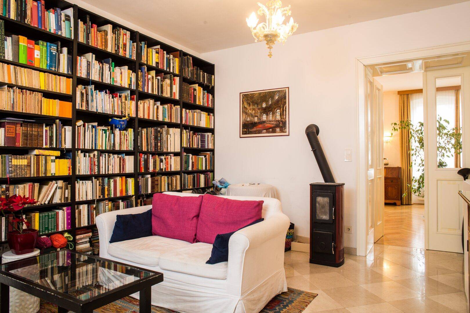 Gemütliches Wohnzimmer mit großem Bücherregal, Kaminofen und hellem Steinboden.