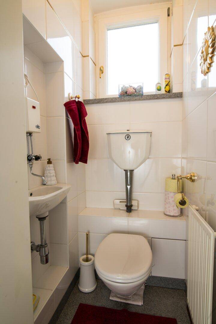 Kleines Gäste-WC mit Fenster, Waschbecken und Wand-WC in weiß gefliestem Raum.