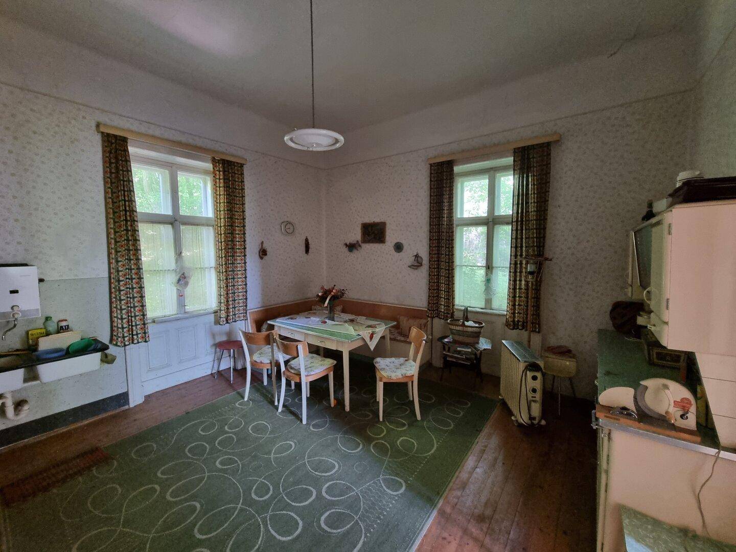 Rustikale Wohnküche mit Essbereich, Teppich und zwei Fenstern, in älterem Zustand.